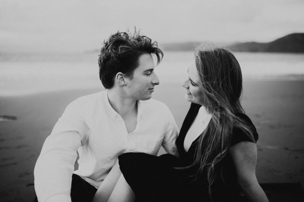 A couple shares a romantic black and white moment on a misty beach at sunset.