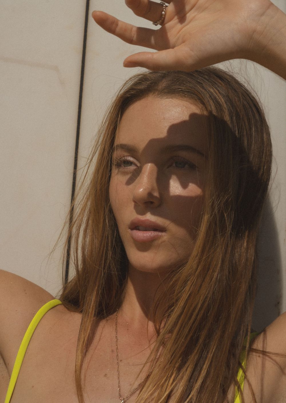 Women posing in the direct sun light, Using her hand to block the sun with a surf bord behind her.
