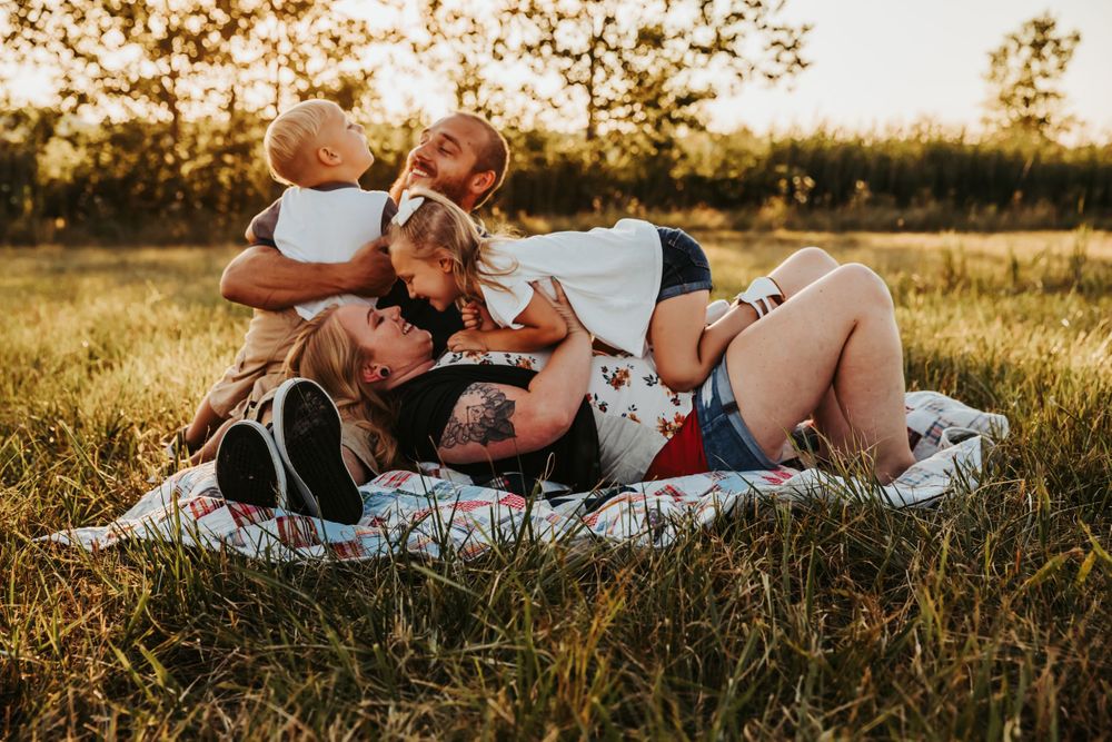 A happy group lying together on a blanket in a sunny meadow during golden hour. terre haute family wedding photographer parke county 478 812
