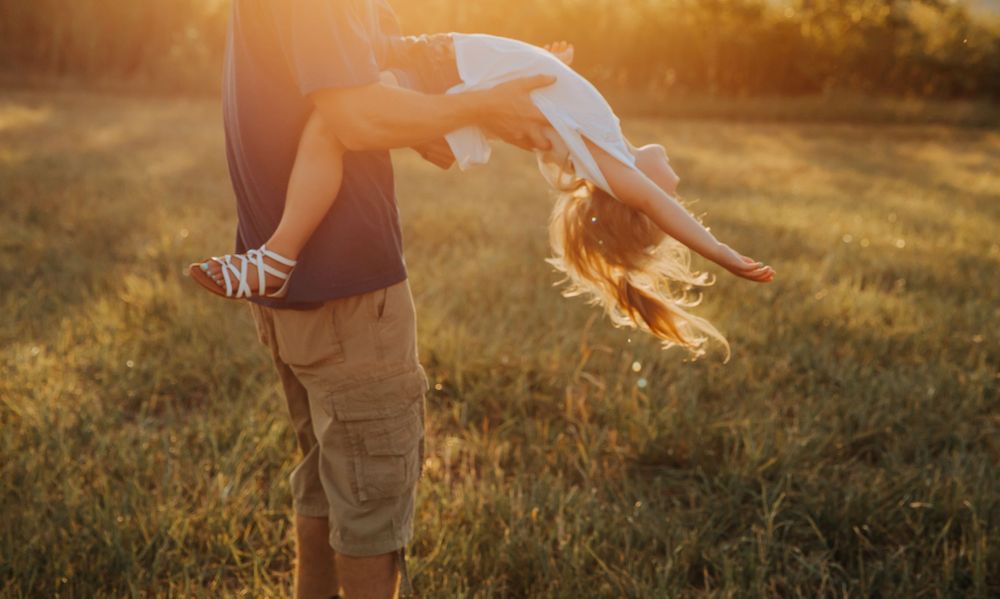 Person in khaki shorts holding a cat in golden sunset light as the cat's fur glows in backlit field setting. terre haute family photos