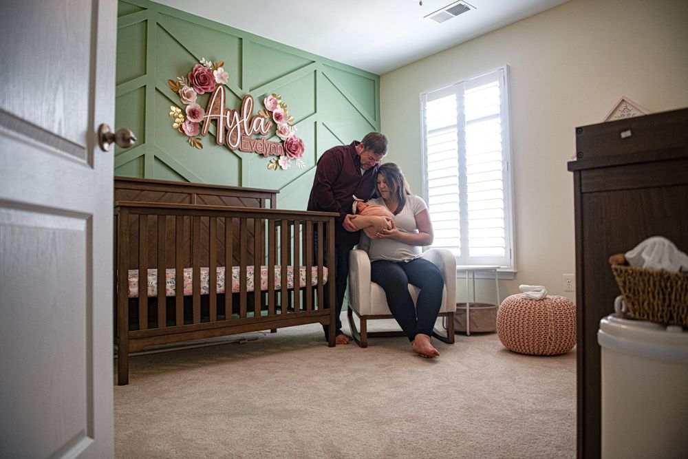A tender moment in a nursery with sage green walls, featuring a wooden crib and woven basket decor.