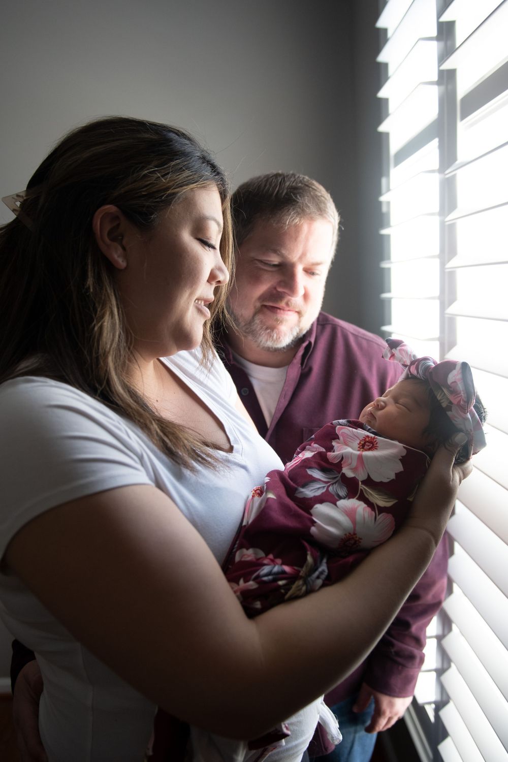 An intimate family moment by a window with venetian blinds casting soft light.