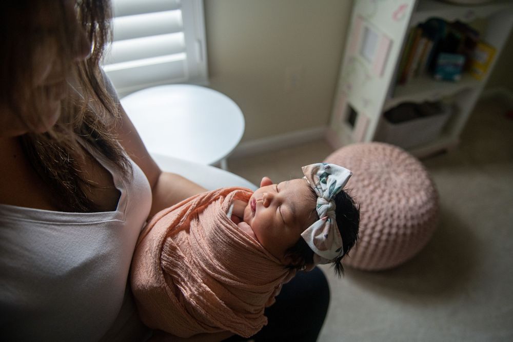 A tender moment with a newborn wrapped in pink against white window blinds.