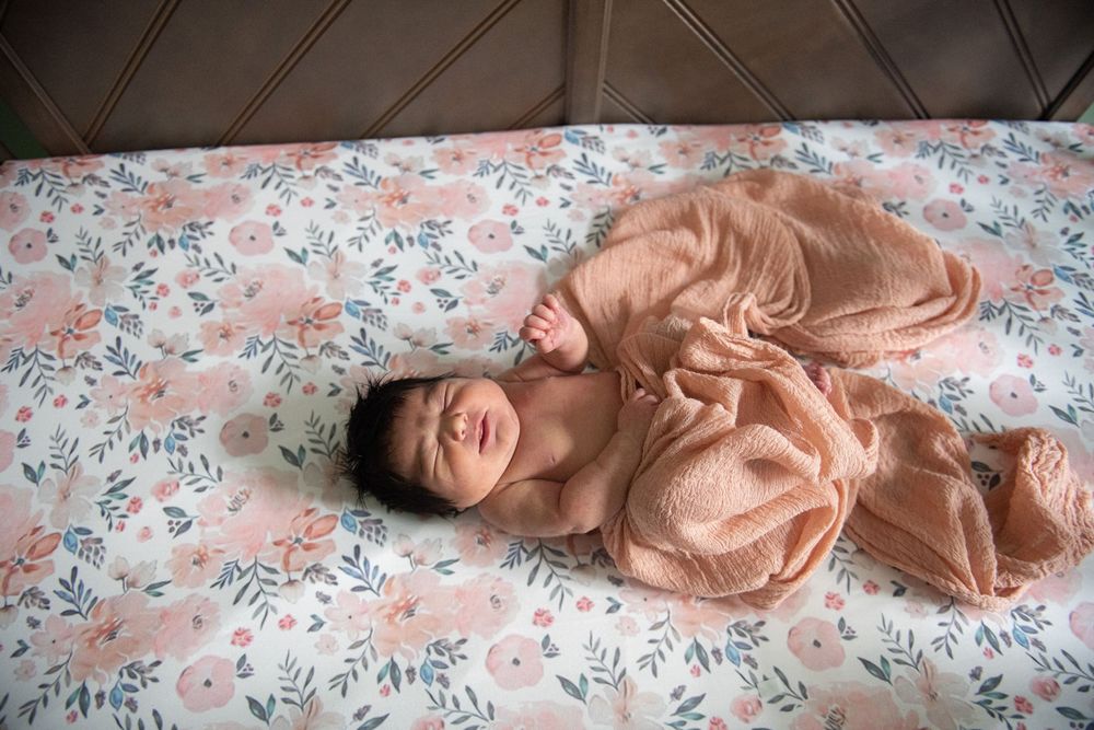 A peaceful newborn in peach-colored wrap rests on floral print bedding.