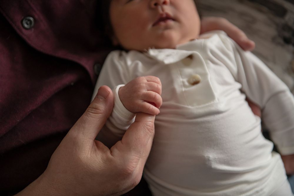 A close-up shot of a tiny hand grasping while wearing a white onesie.