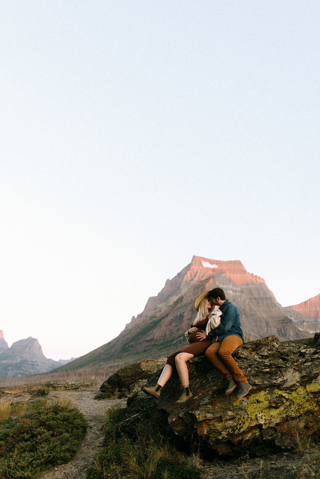 Two hikers climb over rocky terrain at sunset with mountain peaks silhouetted against the sky in the background.