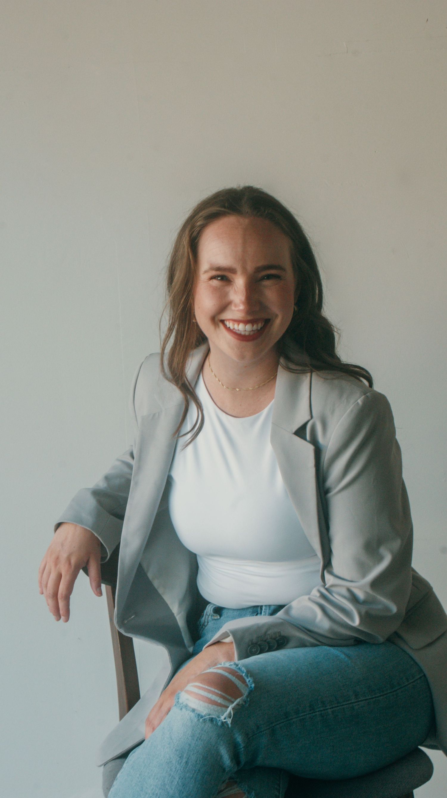 Professional portrait in grey blazer and ripped jeans against minimal background.