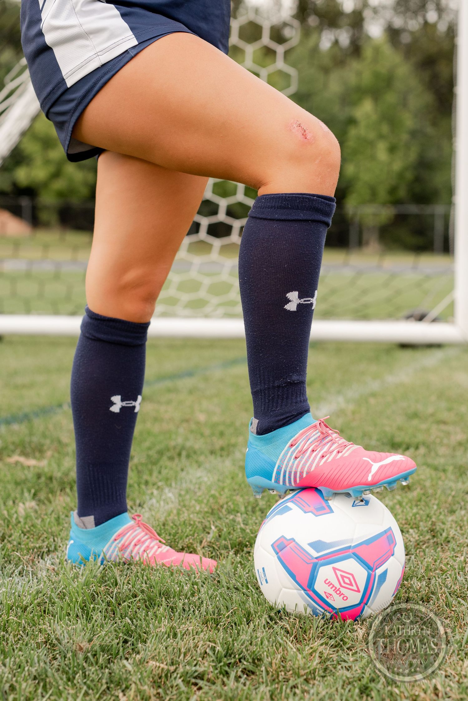 Close up of soccer cleats and Under Armour socks with pink and blue ball.