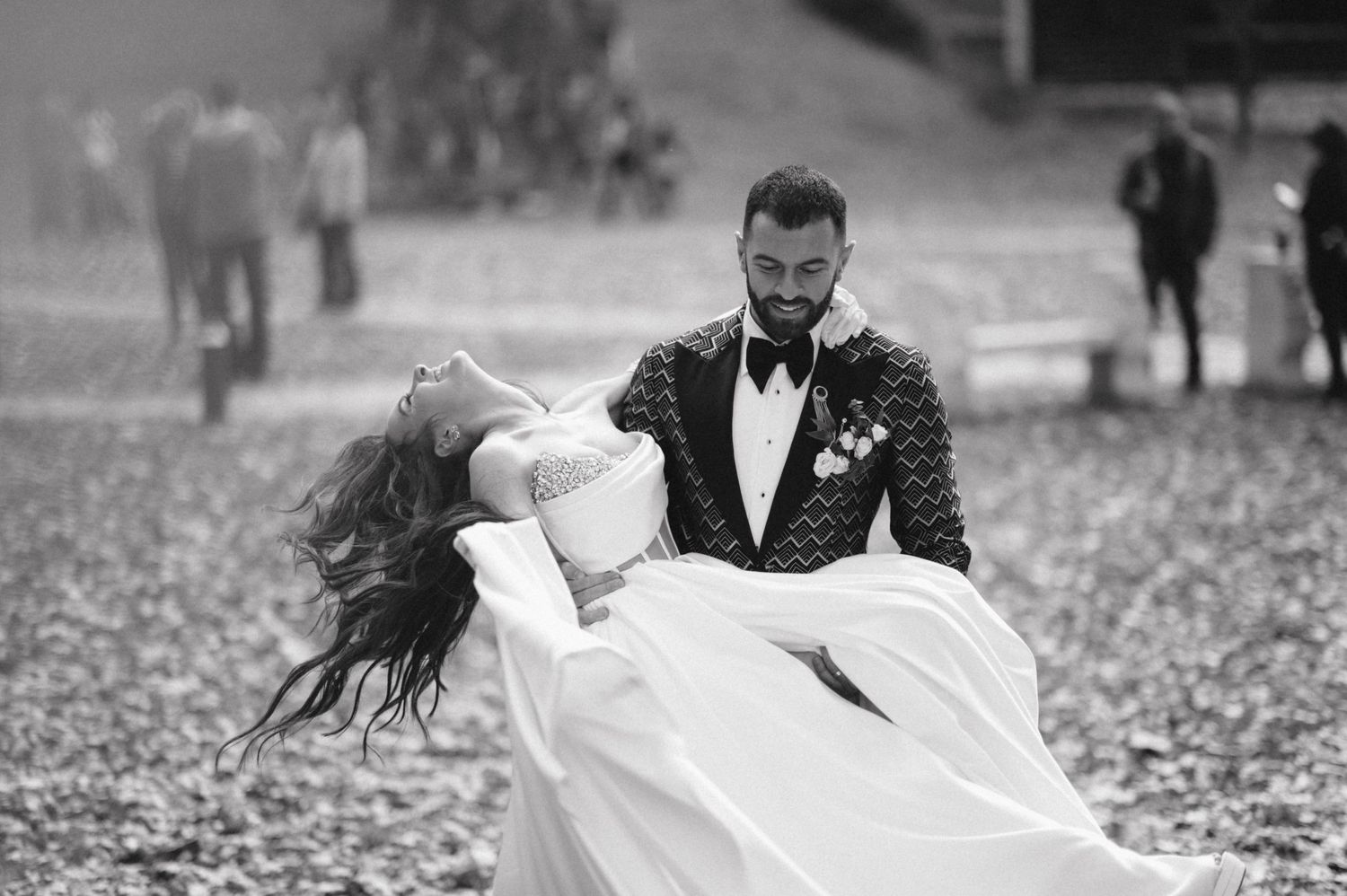 Romantic black and white photo of couple dancing in fallen leaves.
