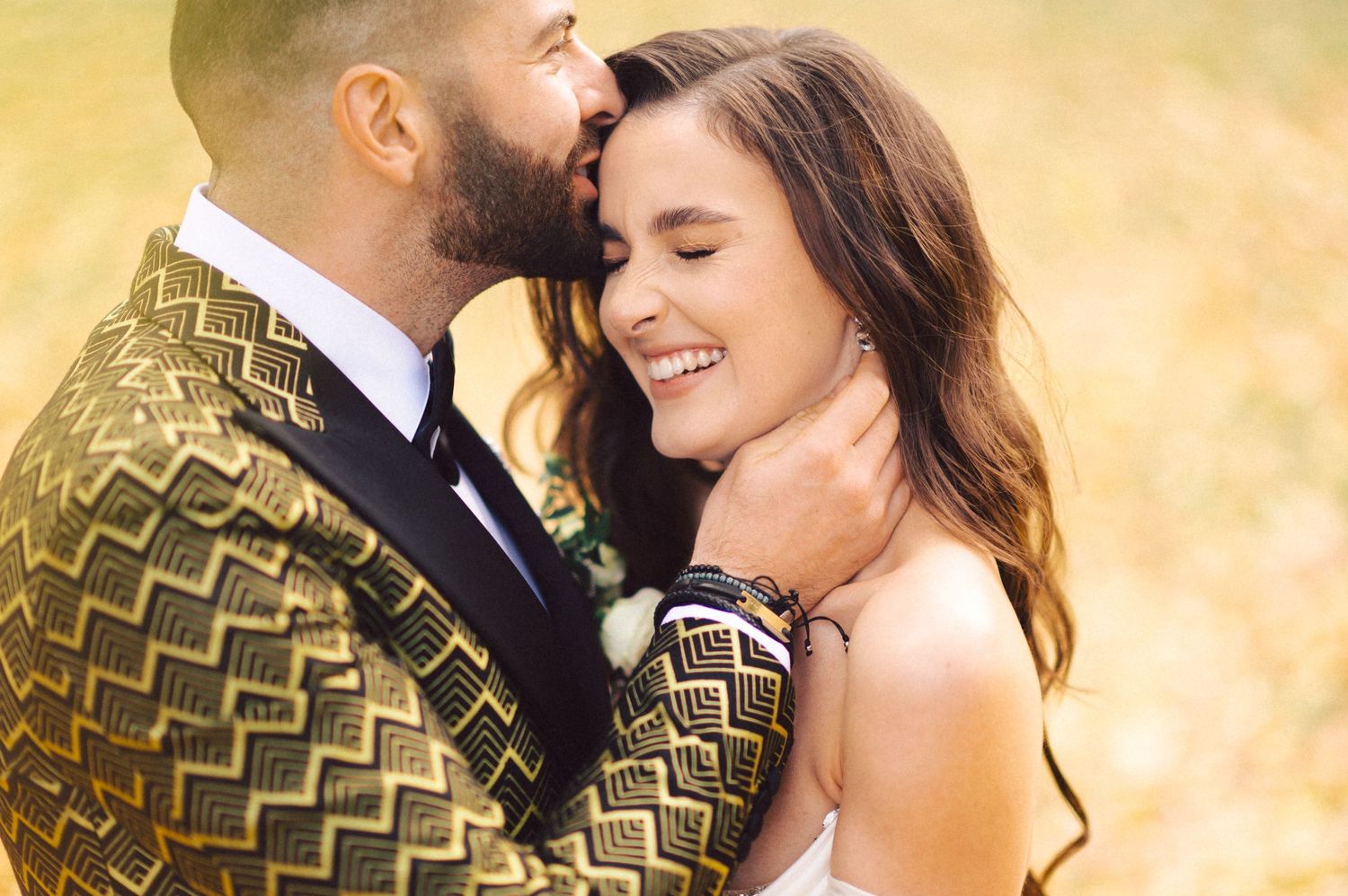 Intimate moment of wedding couple embracing in golden sunlight with autumn colors in background.