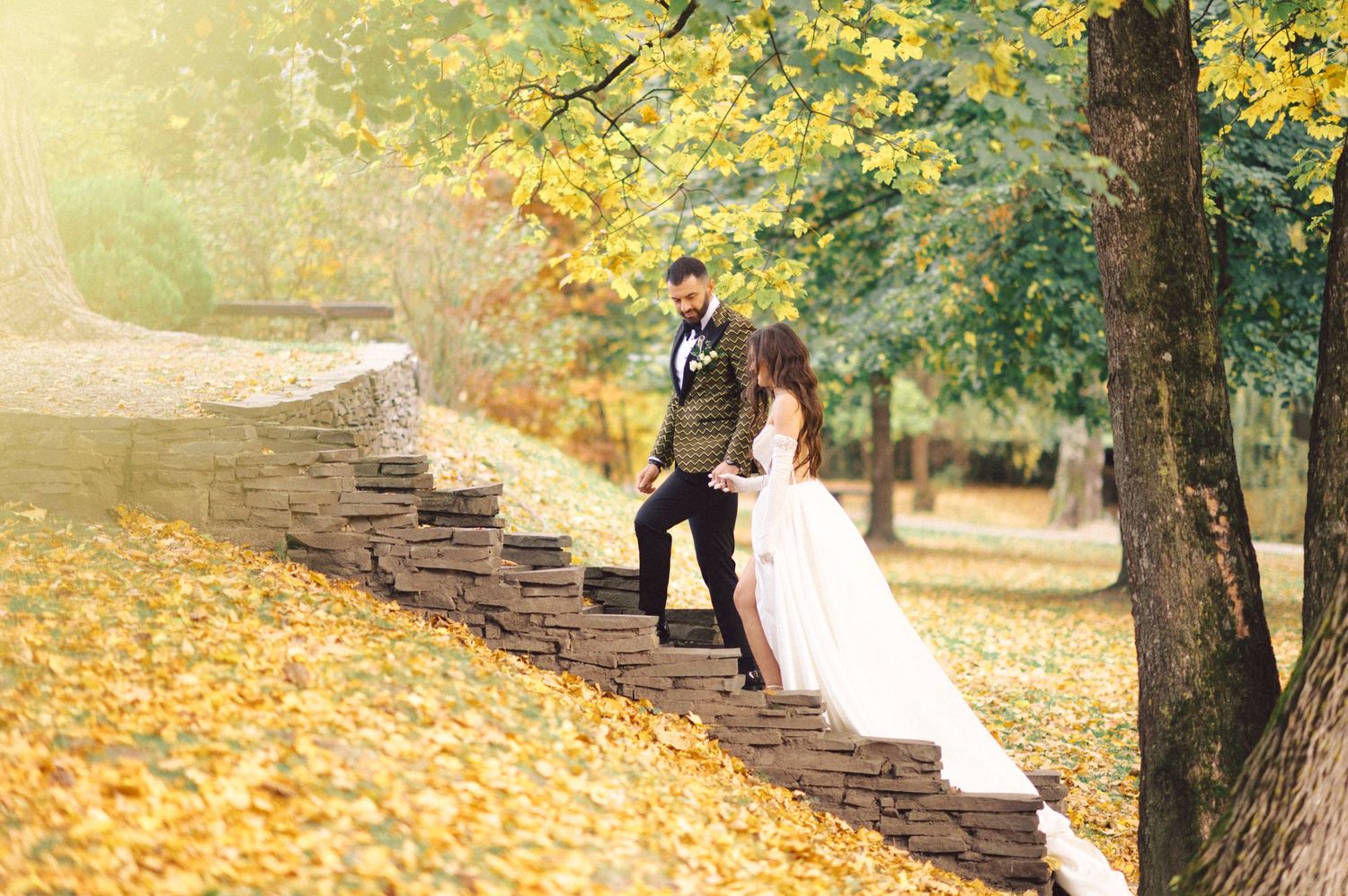 Wedding couple posing on stone steps covered in yellow autumn leaves.
