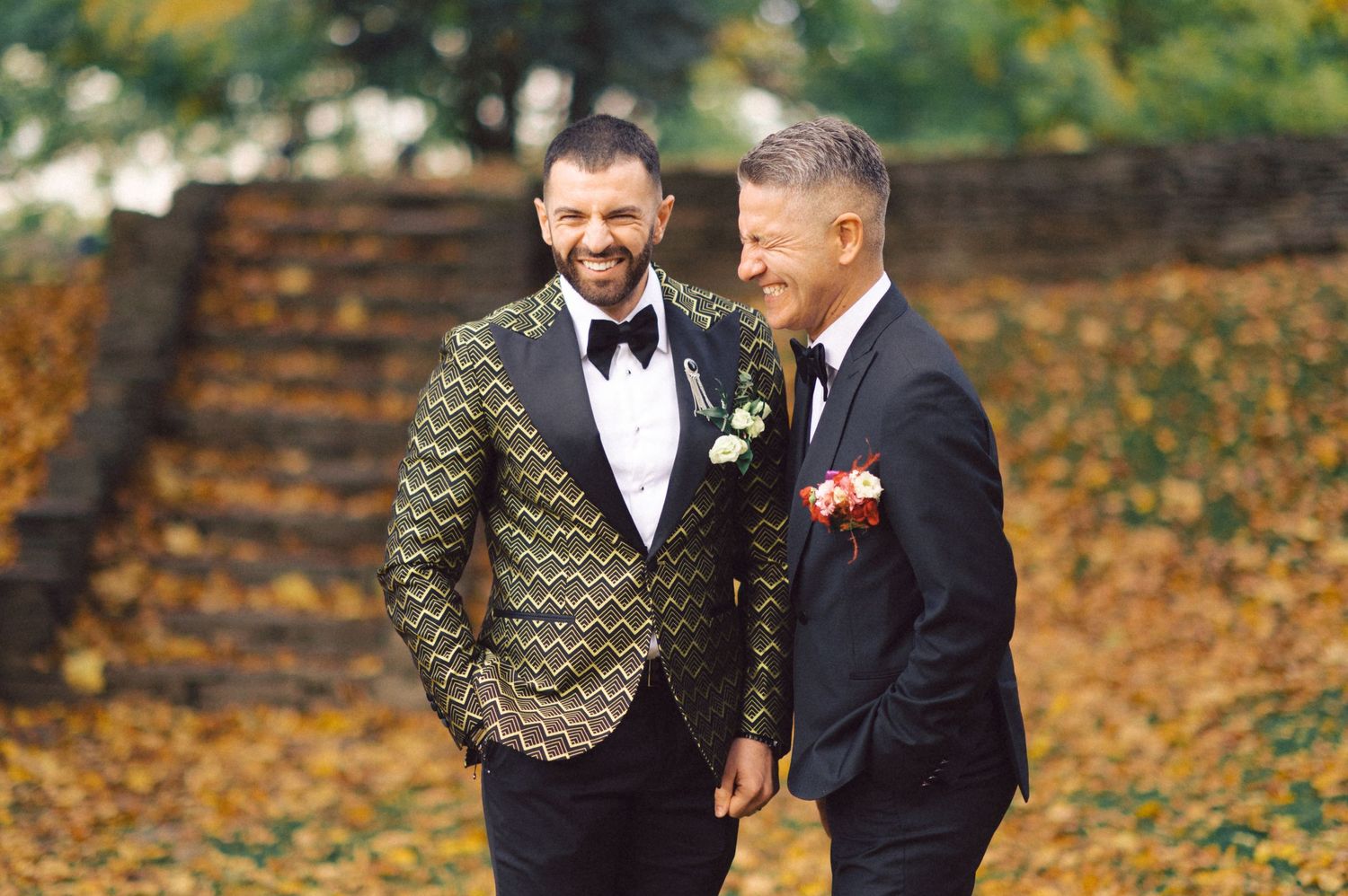 Two people in formal wear sharing joyful moment outdoors in autumn setting.