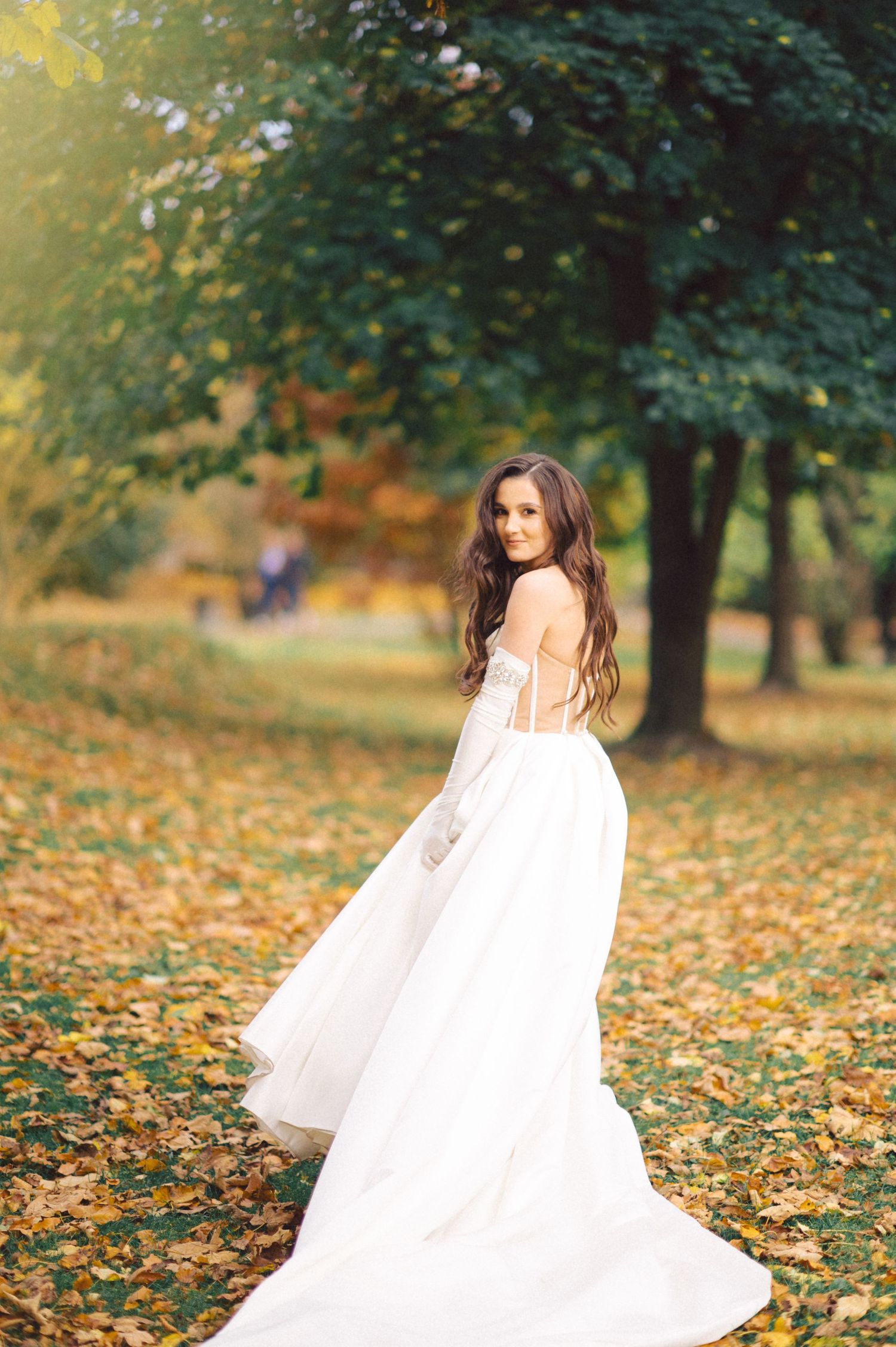 Flowing white wedding dress photographed in autumn park with fallen leaves.