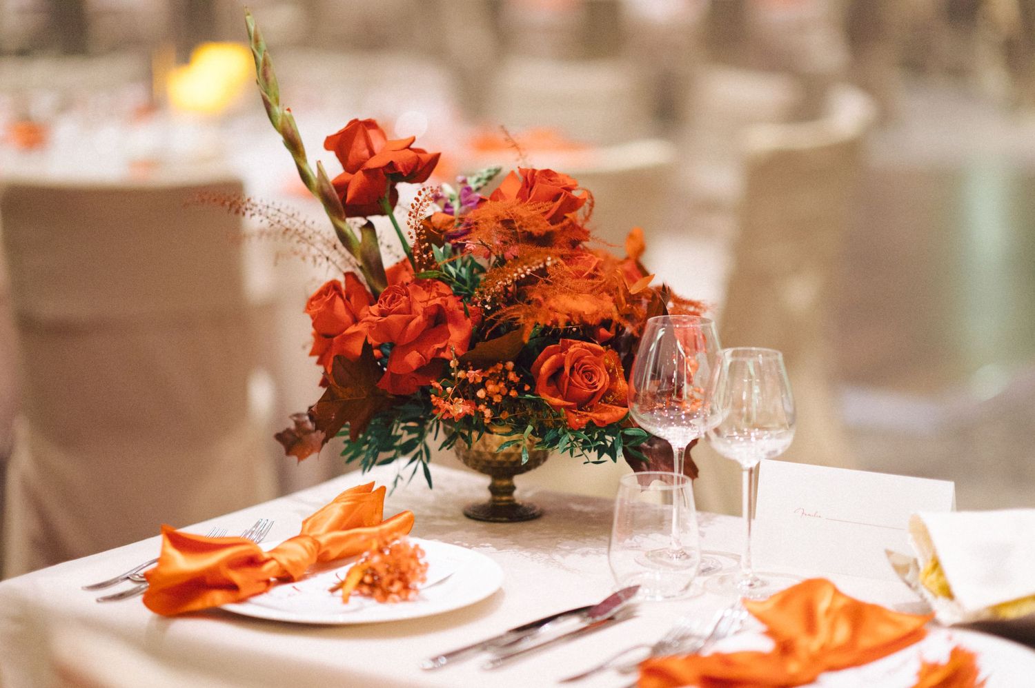 Elegant table setting with vibrant orange and red floral centerpiece and wine glasses.