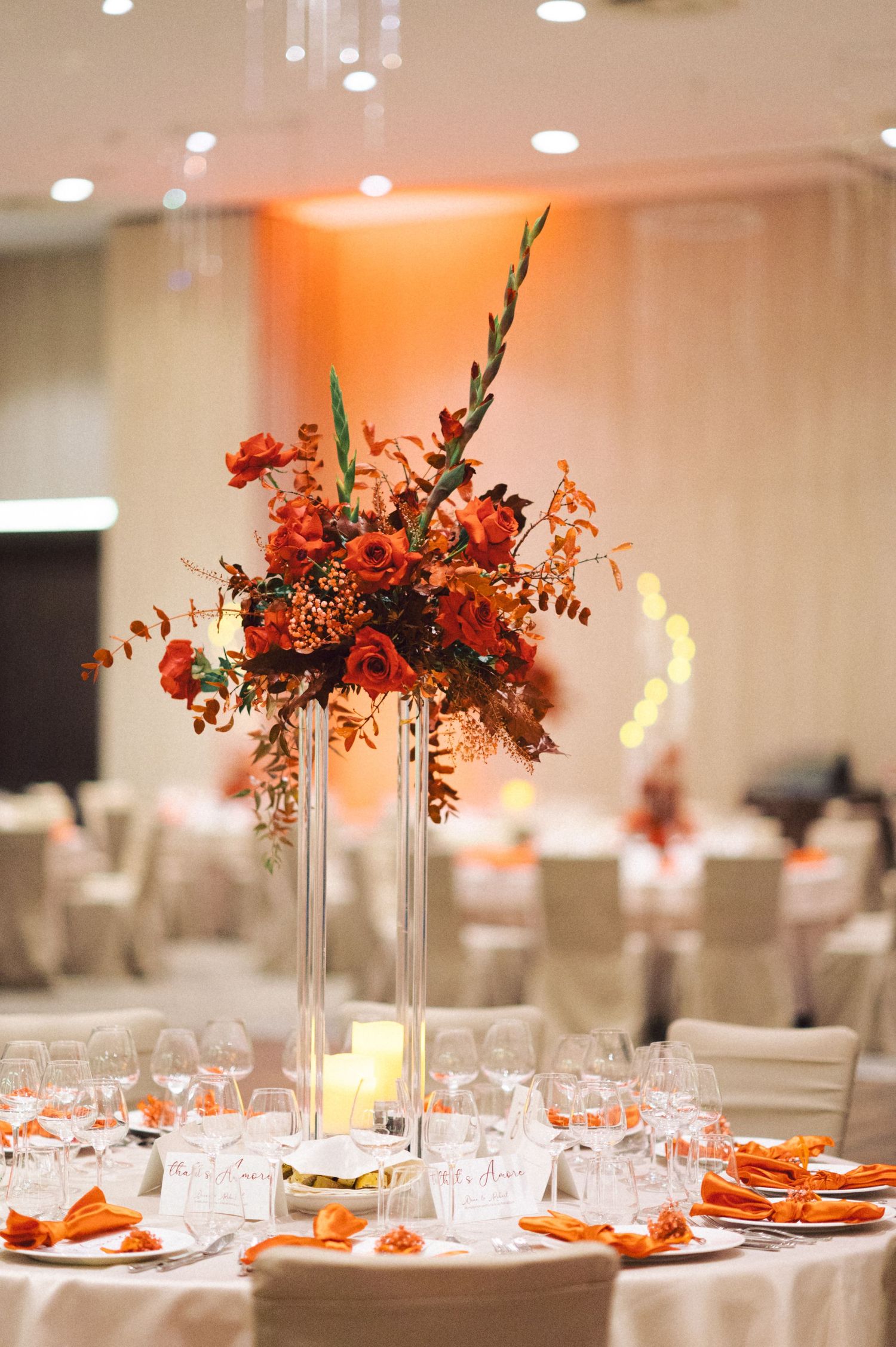 Tall glass vase centerpiece with dramatic orange and red flowers on formal reception table.