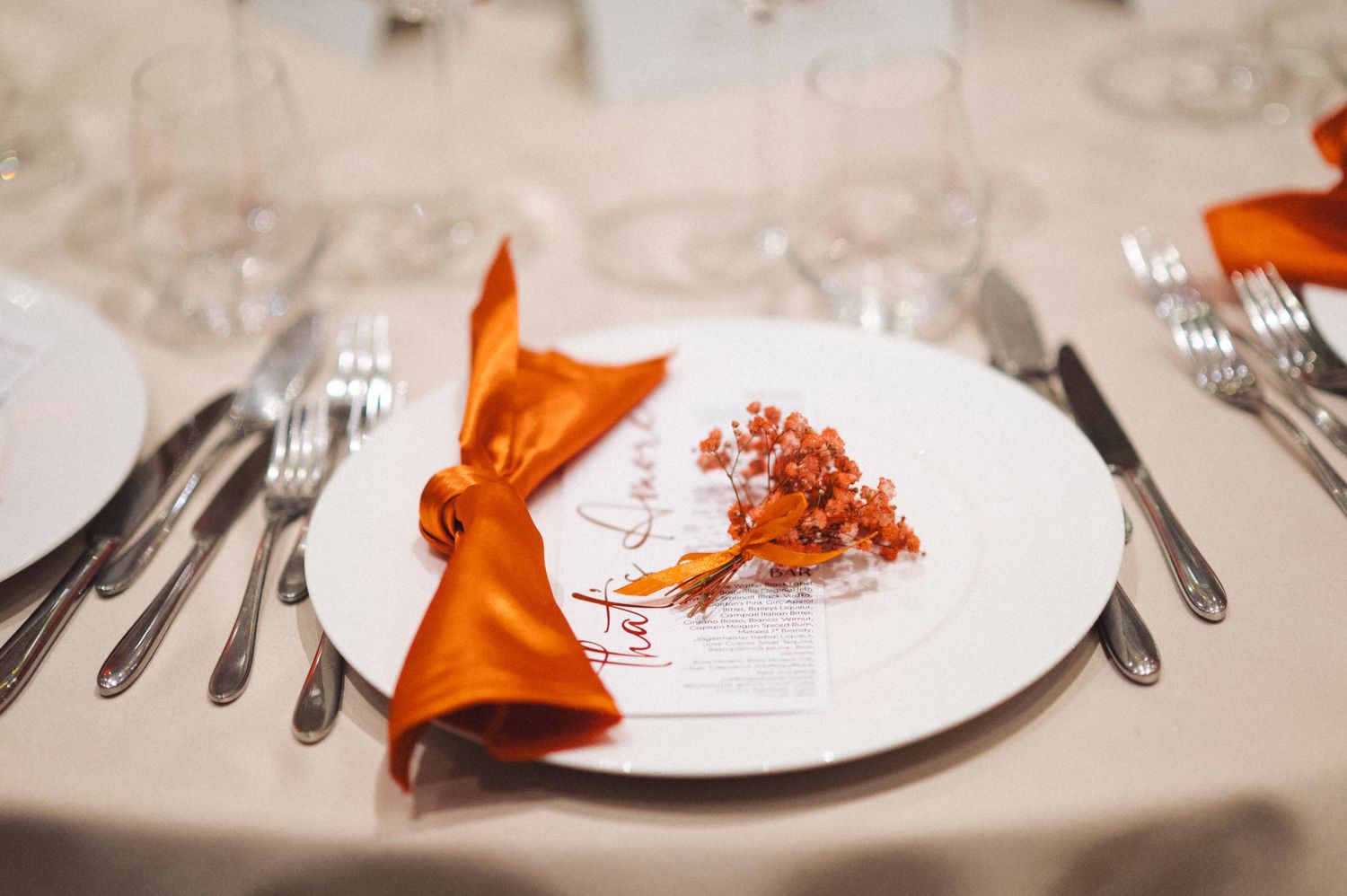 White plate place setting with bright orange napkin and delicate floral accent.