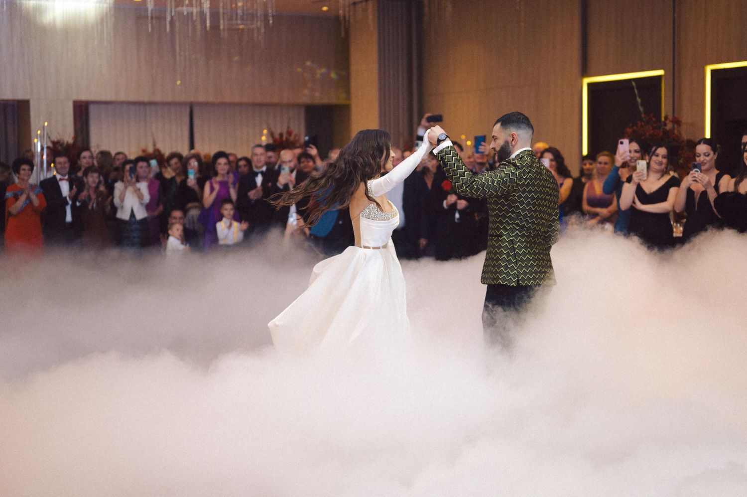 A couple performs their first dance at a wedding reception with dramatic fog effects on the dance floor.