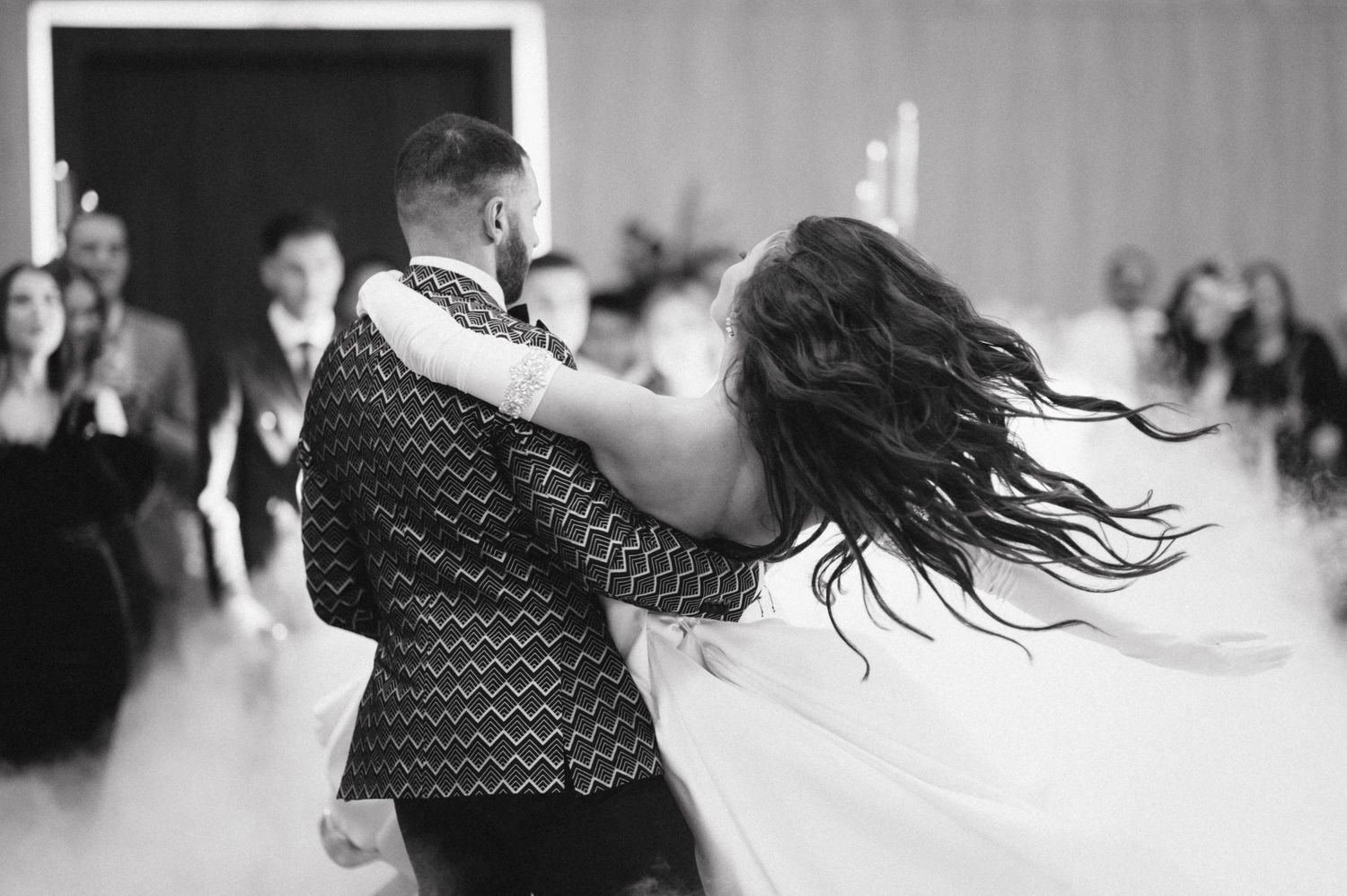 A bride and groom share an energetic dance moment in black and white at their wedding reception.