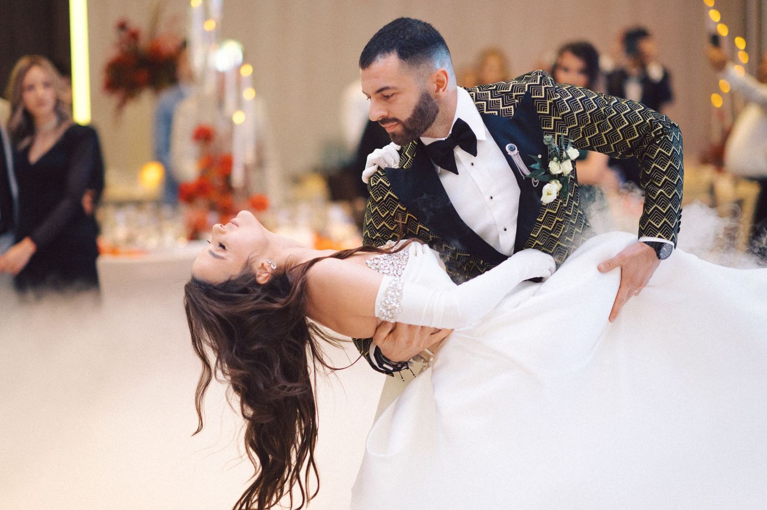 A couple performs a dramatic dip during their wedding dance on a misty dance floor.