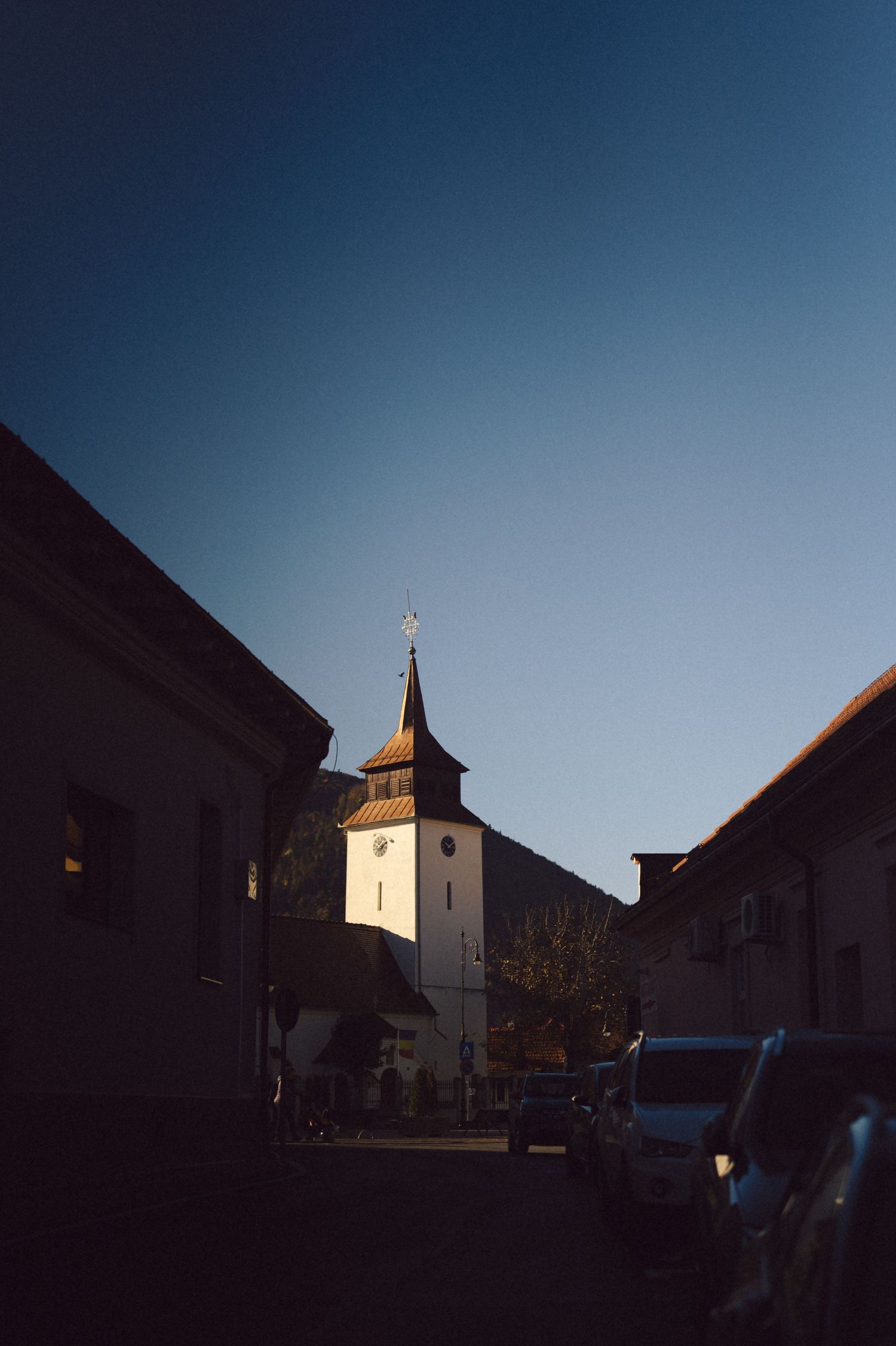 A church steeple rises against a deep blue sky between buildings at dusk.