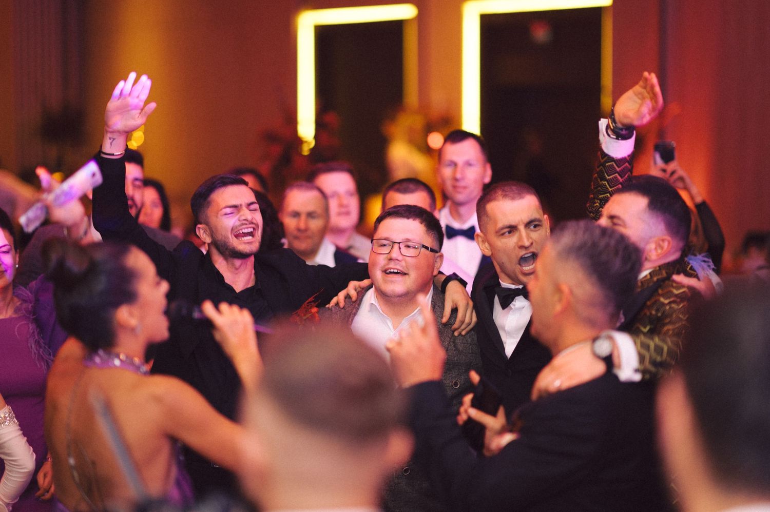 Energetic wedding reception crowd cheering and dancing together on the dance floor.