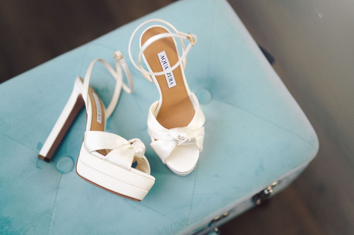 Elegant white bridal shoes with high heels on blue surface.