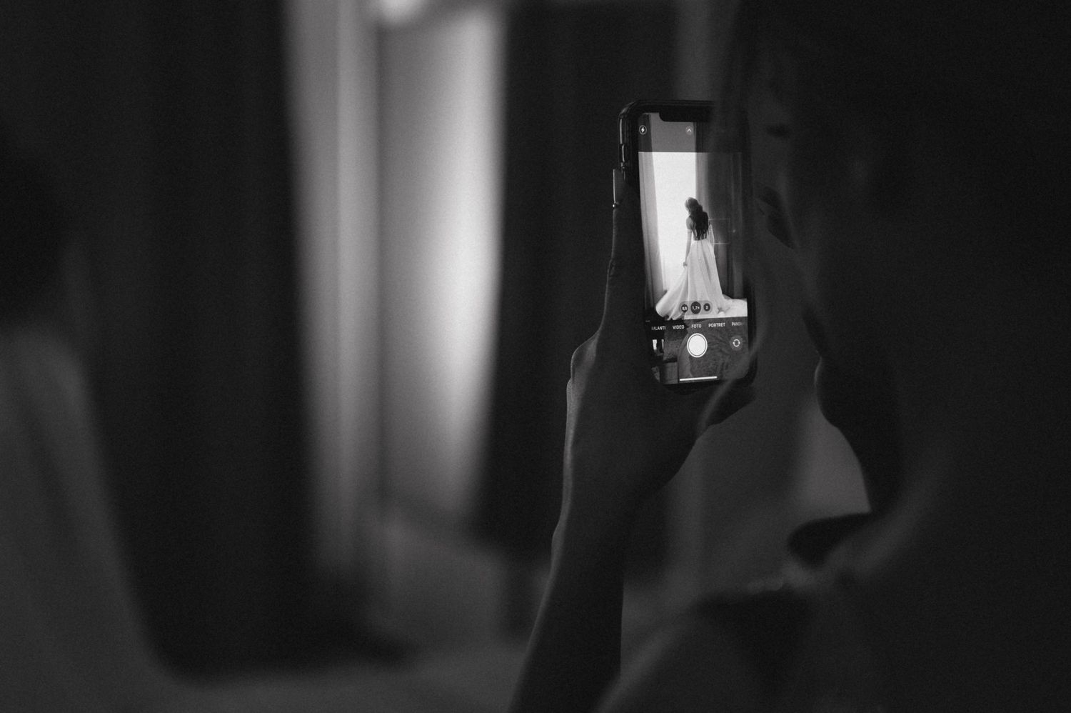 A silhouetted hand holds up a phone capturing a photo in dark dramatic lighting.
