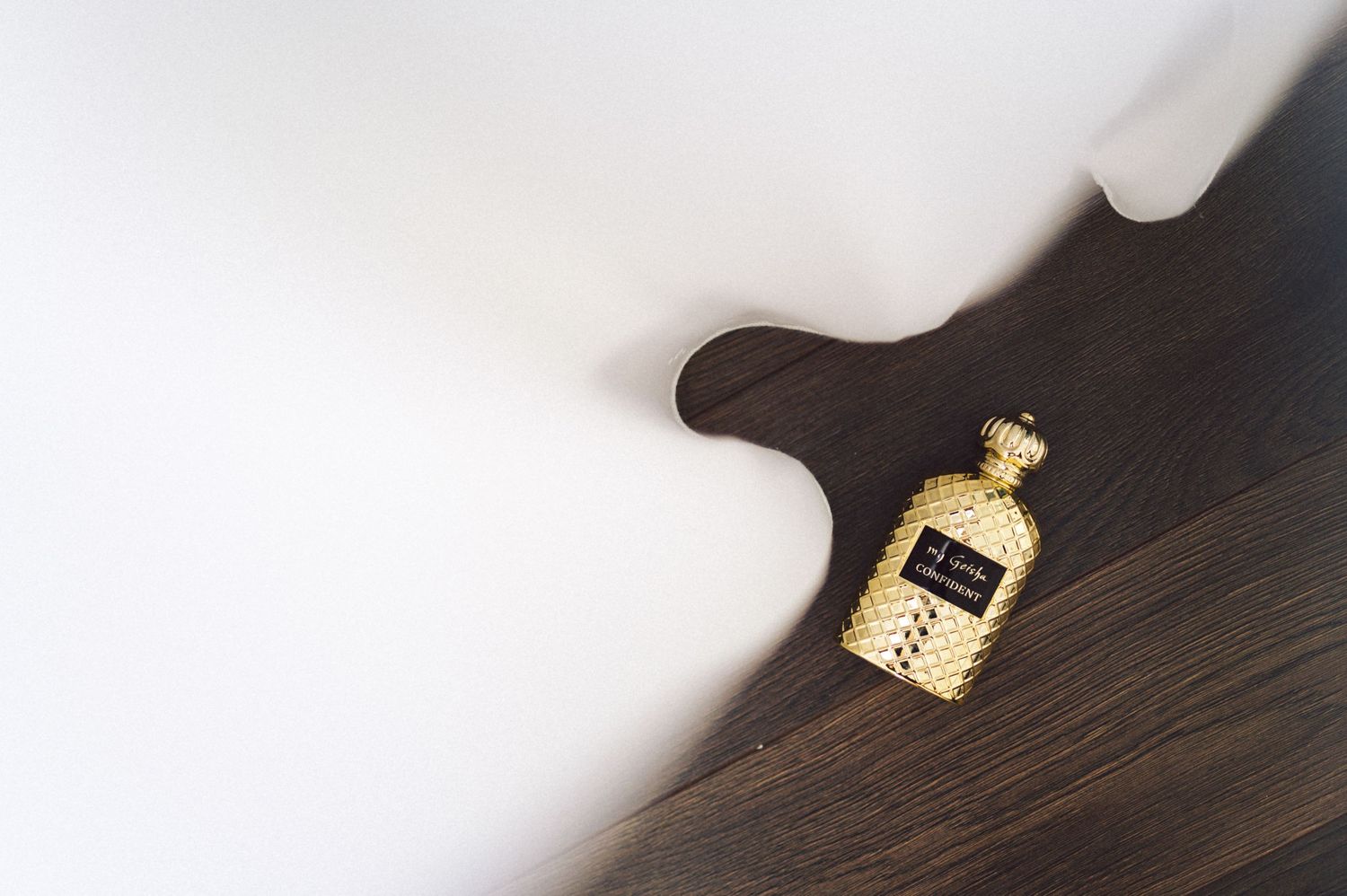 Small perfume bottle on dark wooden surface with dramatic lighting.