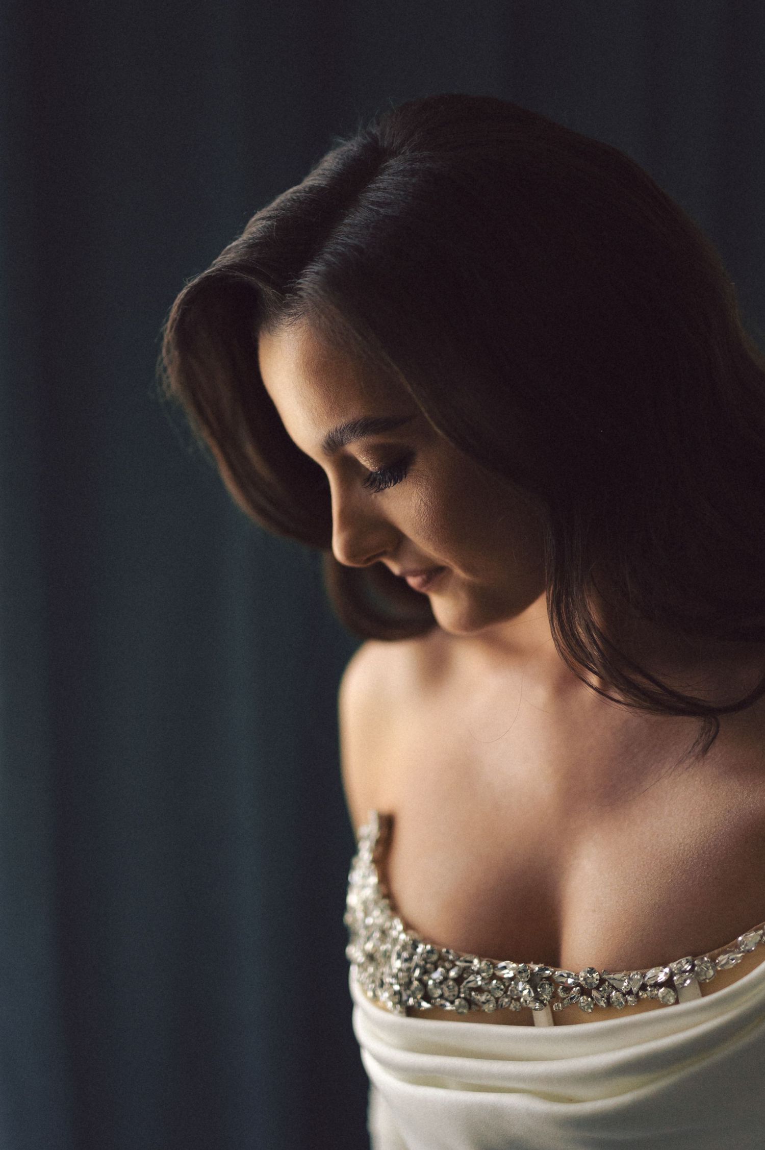 A soft portrait showcases an ornate beaded neckline of a wedding dress in dramatic lighting.