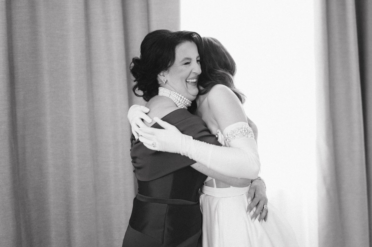 Two women share an emotional embrace in formal dresses during what appears to be a wedding celebration.