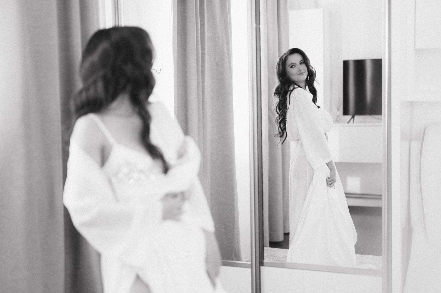Elegant bride in white dress gazes at her reflection in a mirror during wedding preparations.