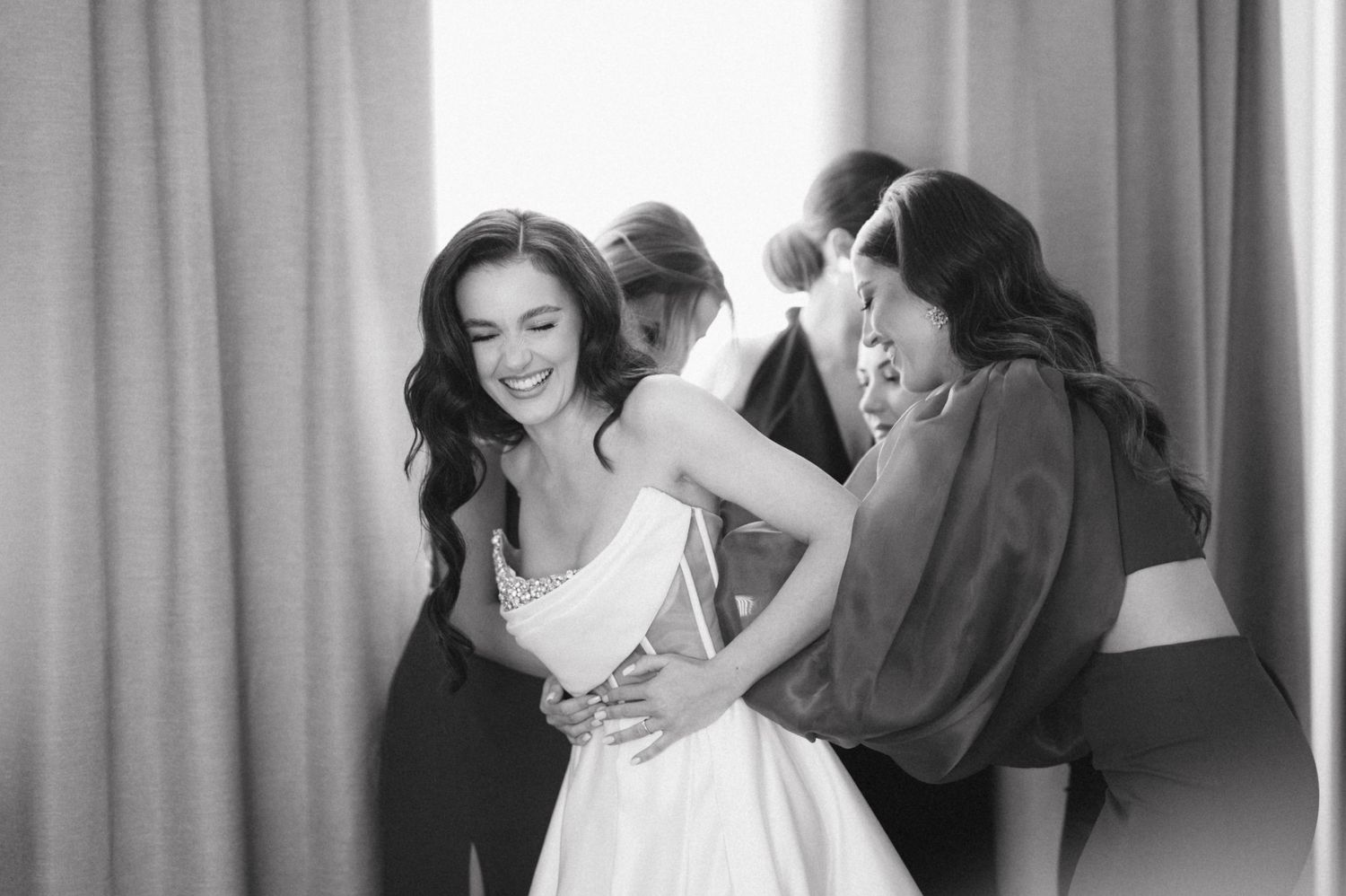 Black and white photo of joyful wedding party getting ready in a bright room.