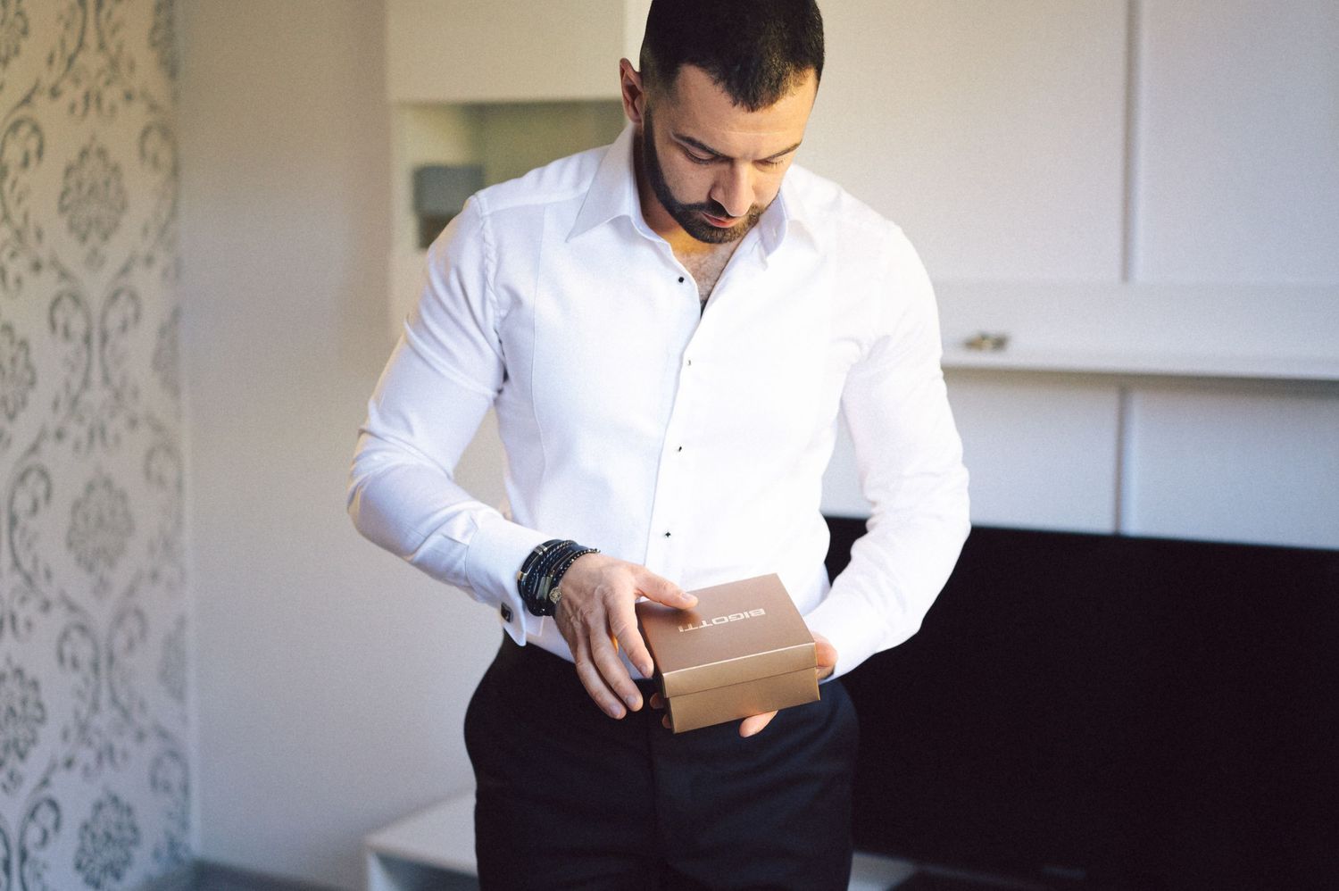 A man in a crisp white shirt checks his watch while getting dressed for a formal event.