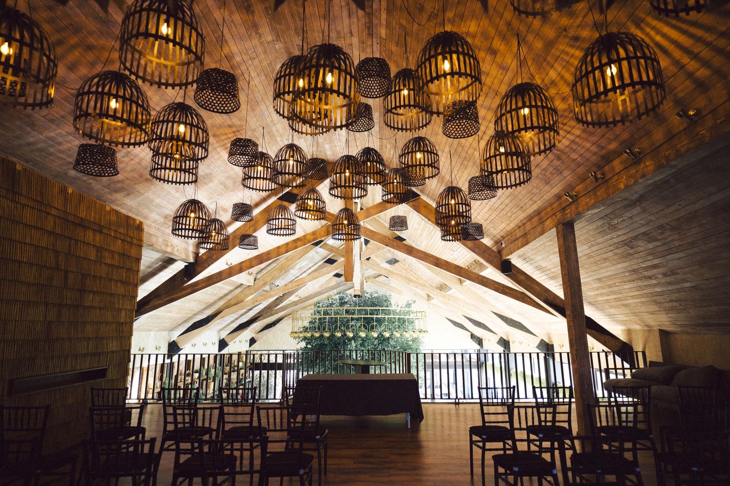 A rustic wedding venue interior decorated with hanging wicker lanterns and wooden beams.