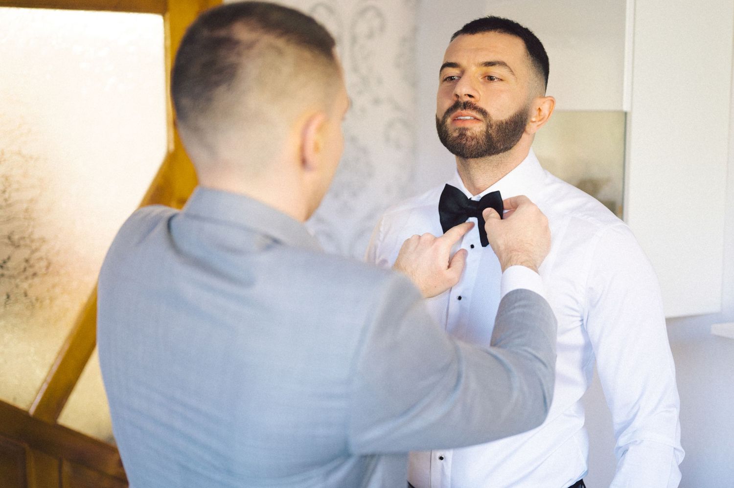 Someone helps adjust a black bow tie on a white dress shirt during wedding preparations.