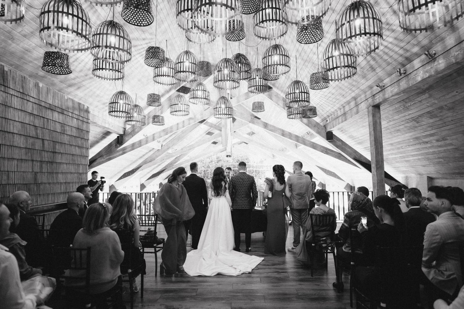 A black and white wedding ceremony under hanging lanterns in a rustic venue.
