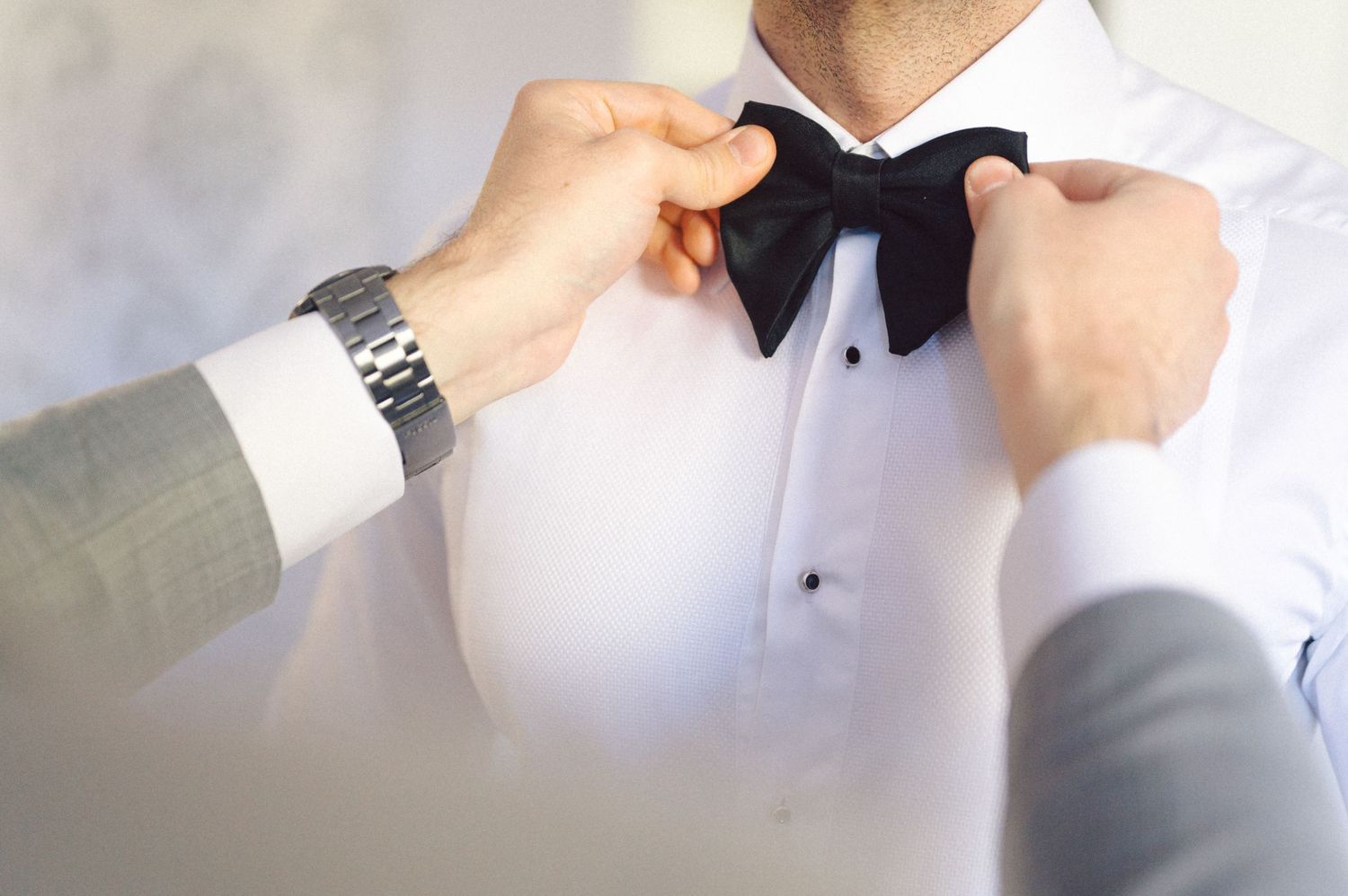 Hands adjust a classic black bow tie on a white tuxedo shirt.