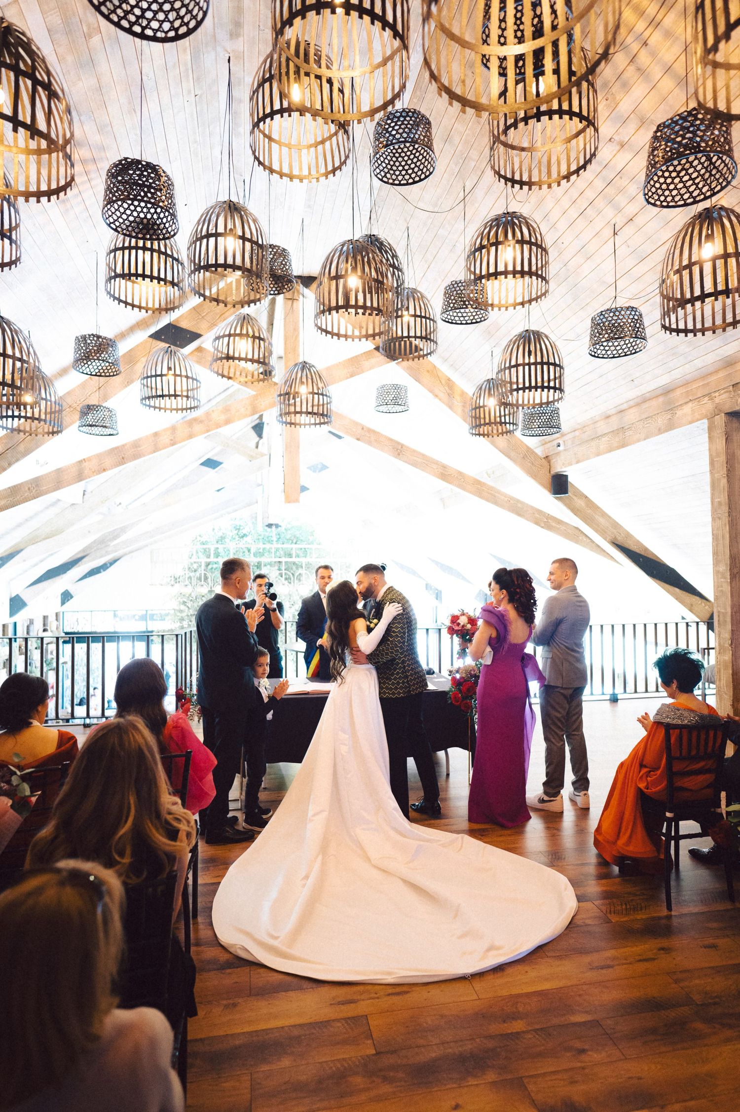 Wedding ceremony under decorative woven basket light fixtures in a rustic wooden venue.