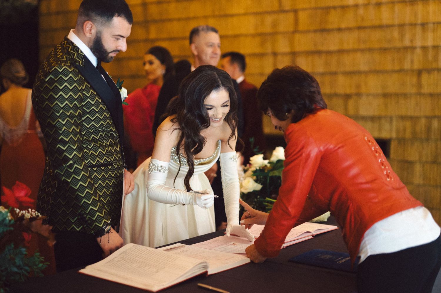 Wedding ceremony participants sign official documents at a wooden table during the celebration.