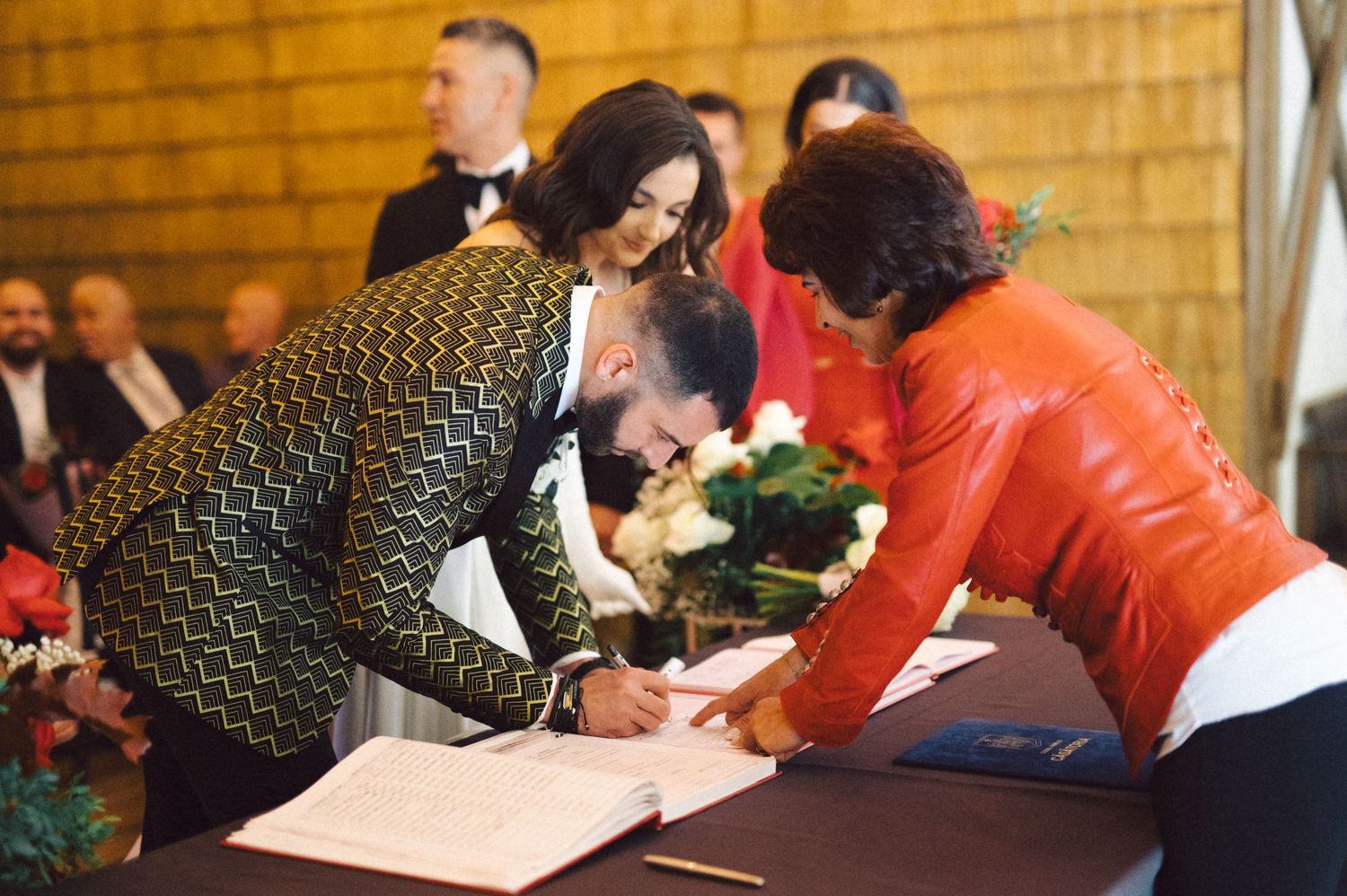 Wedding participants signing marriage documents at a wooden table during the ceremony.