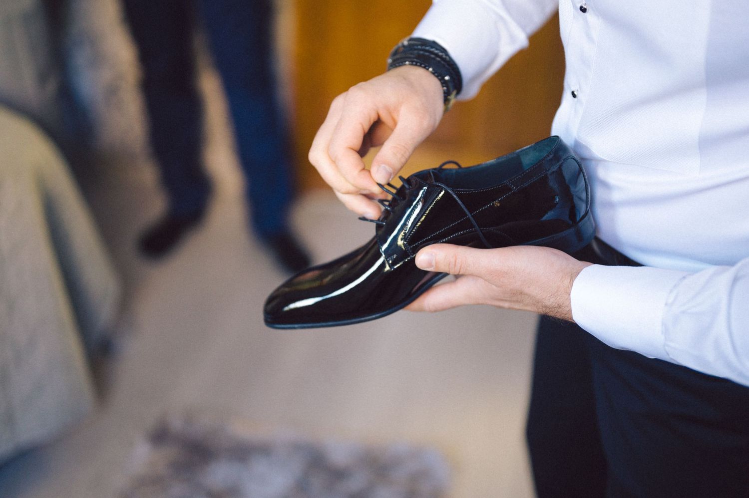 Close-up of hands holding a shiny black formal dress shoe during wedding preparations.