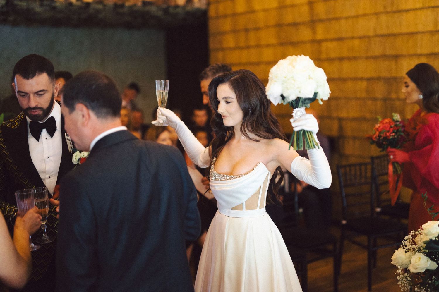 Bride in white dress holds bouquet while celebrating at wedding reception.