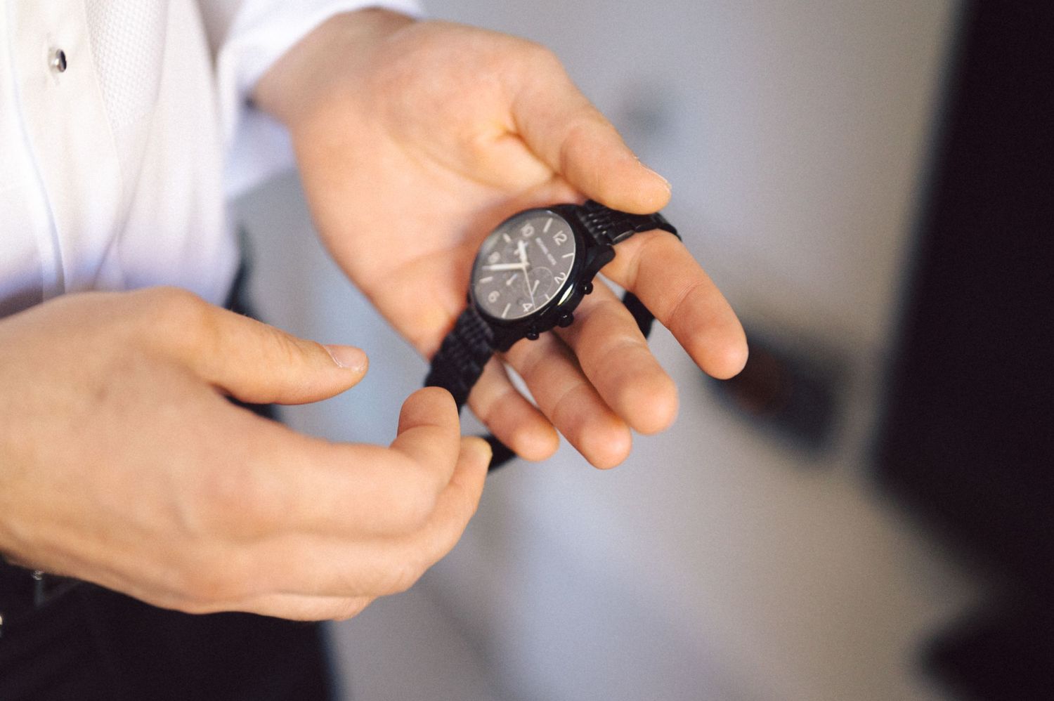 Hands adjusting an elegant black watch during formal event preparations.