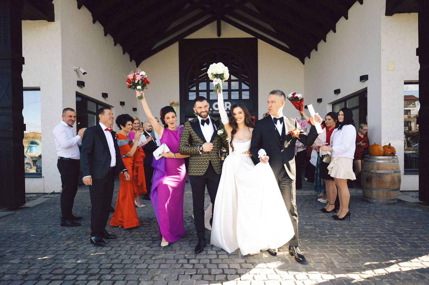 Wedding party celebrating outside venue entrance with colorful attire and festive poses.