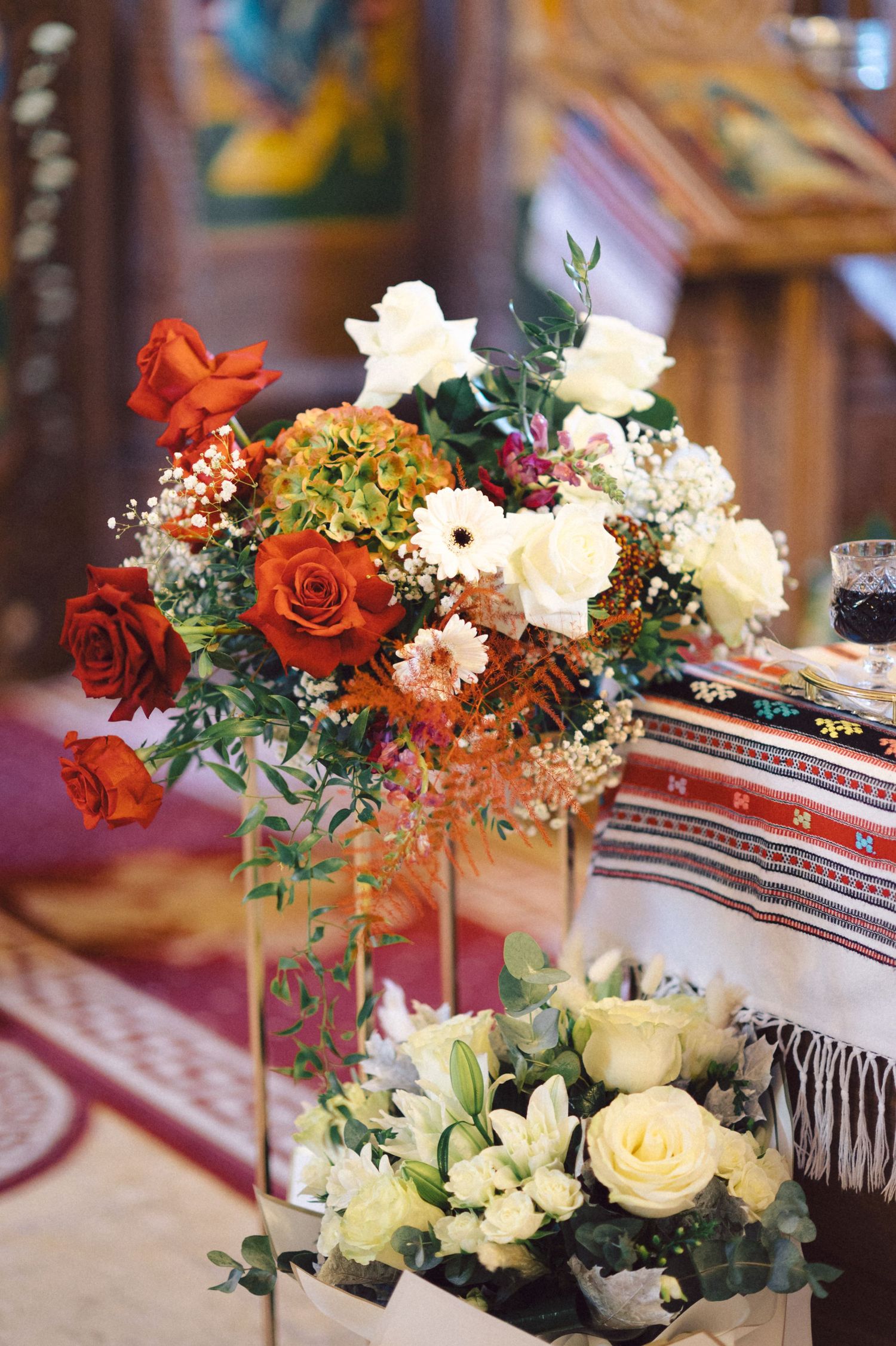 Elegant floral centerpiece with red and white roses on traditional patterned tablecloth.