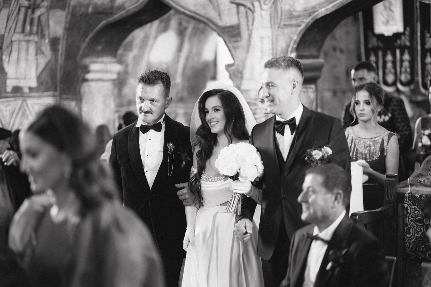 Black and white photo of formal wedding reception guests in elegant venue setting.