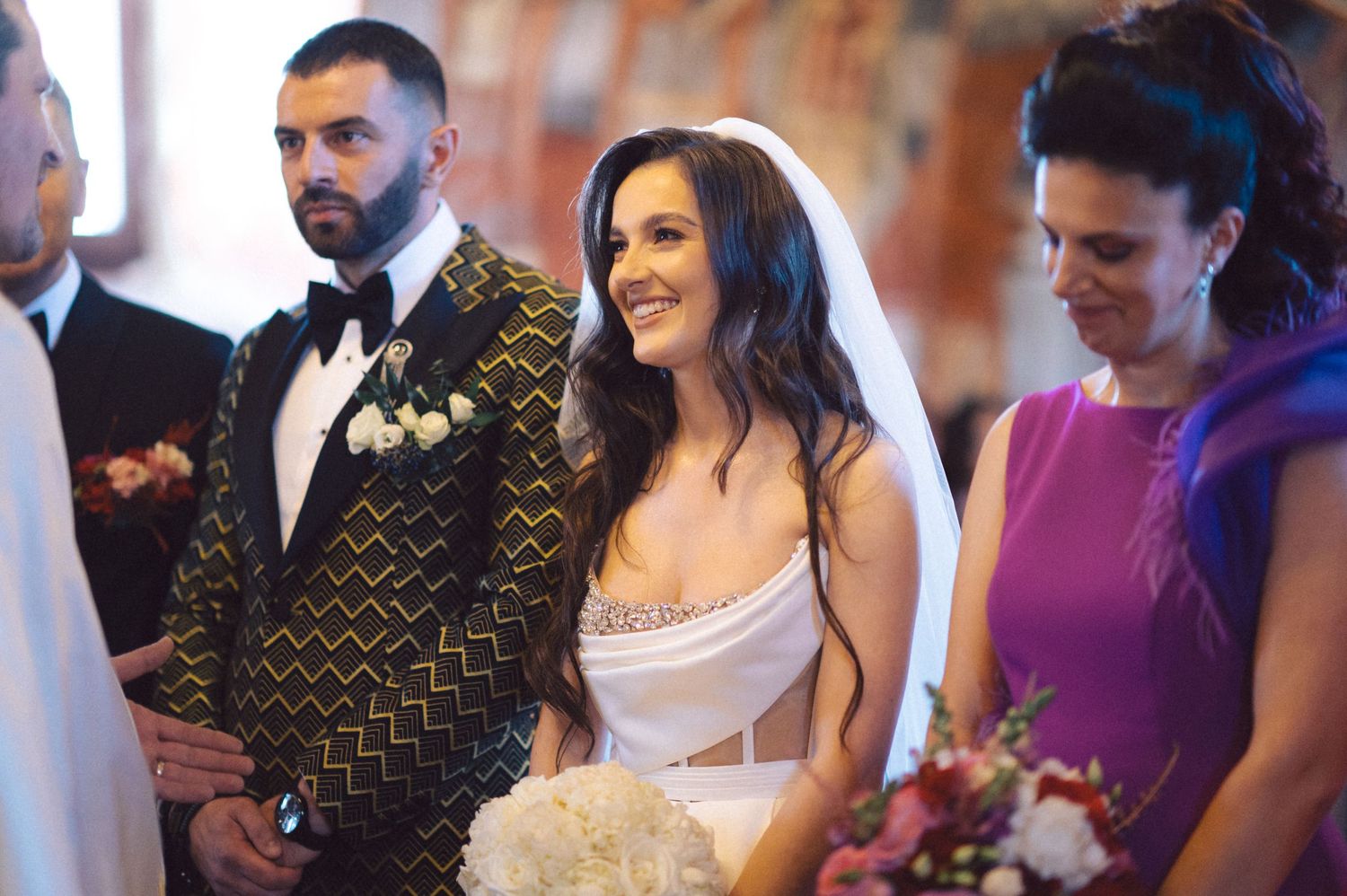 A wedding ceremony in process with the couple and guests standing in an ornate church setting.