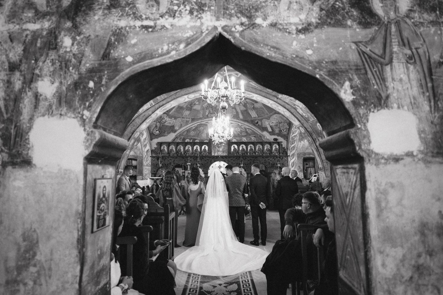 A dramatic black and white shot of a wedding ceremony under an ornate church archway with guests watching.