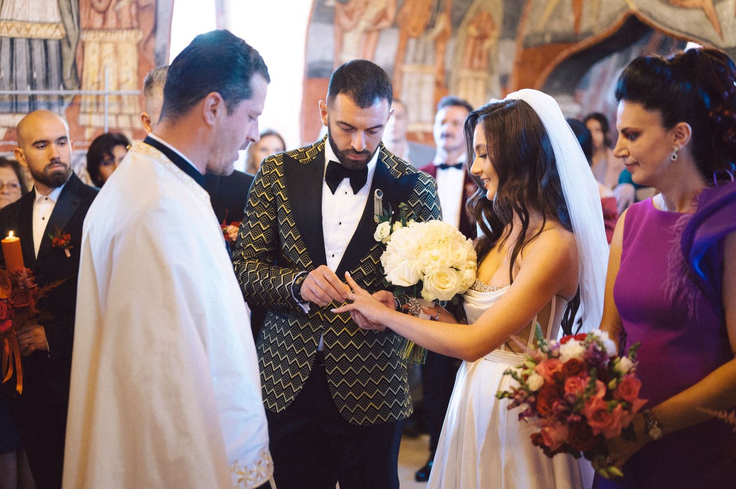 Wedding ceremony moment with couple and officiant exchanging rings in an ornate church setting.