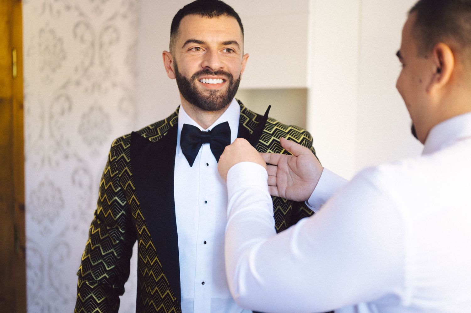A formal occasion showing the adjustment of a boutonniere on a gold patterned tuxedo jacket.